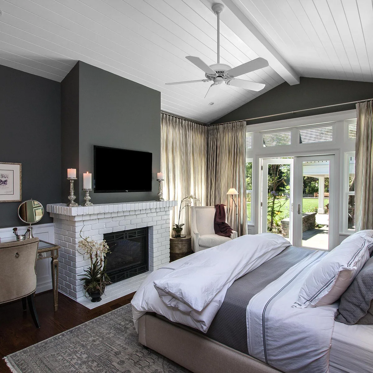 Grey bedroom walls above a white brick fireplace beside pale bedding and light curtains