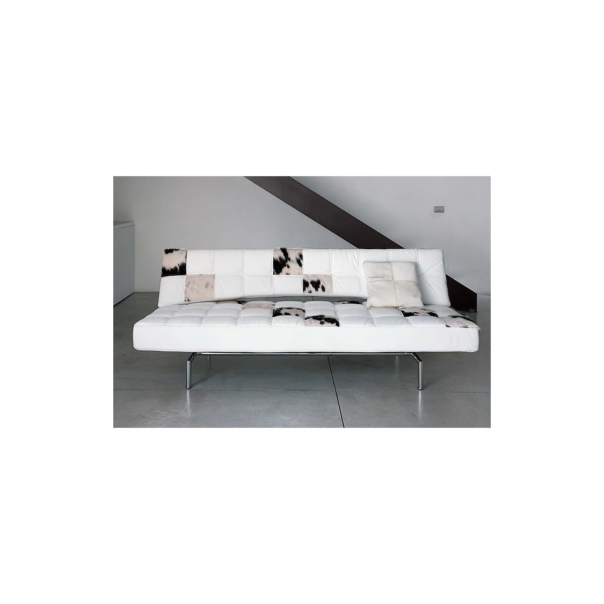 White armless sleeper sofa with patchwork-style dark accents and slim metal legs