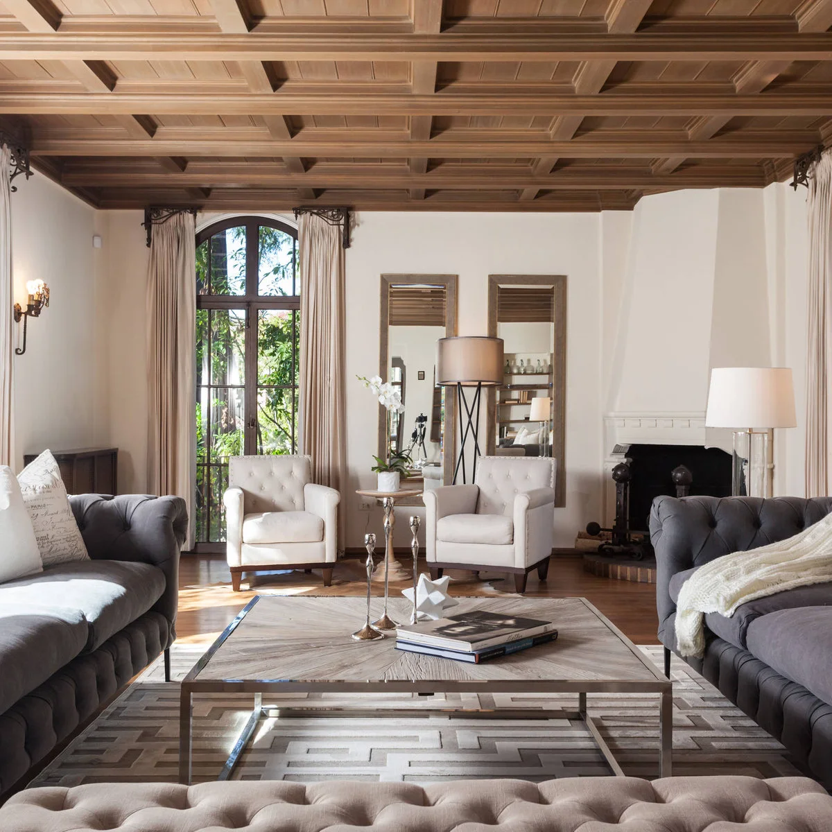 Two gray tufted sofas face across a square table, with pale armchairs at the far end and a low upholstered seat in front.