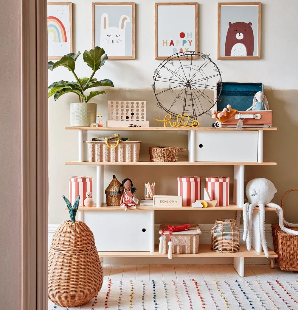 Low wood and white storage unit with baskets, striped tins, games, dolls and a large woven floor basket