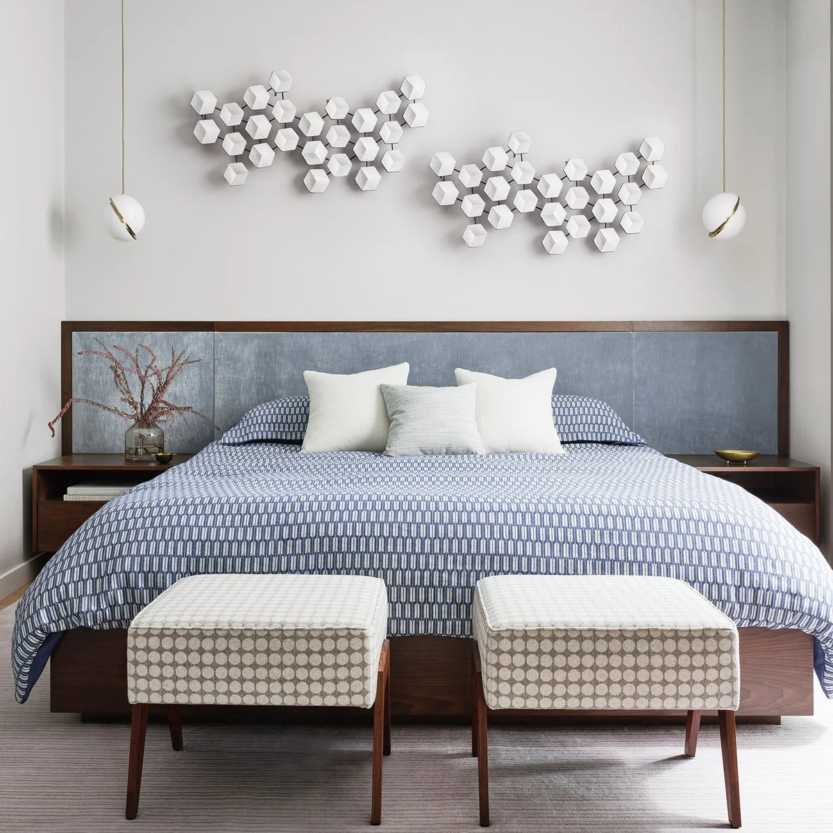 Two clusters of white faceted geometric wall ornaments above a broad blue-gray headboard with pendant lights.