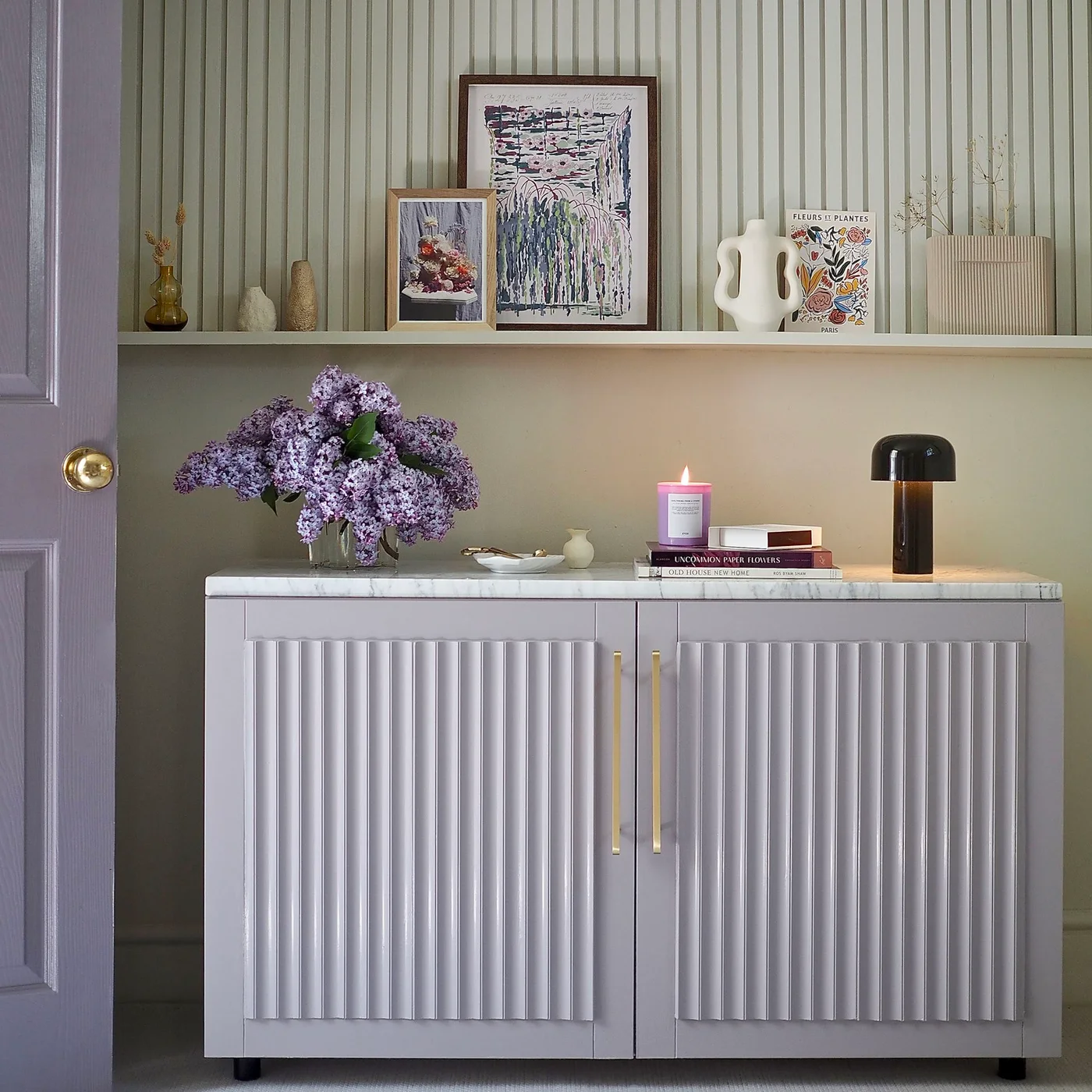 Lilac cabinet with fluted doors, gold-colored handles and a pale patterned top