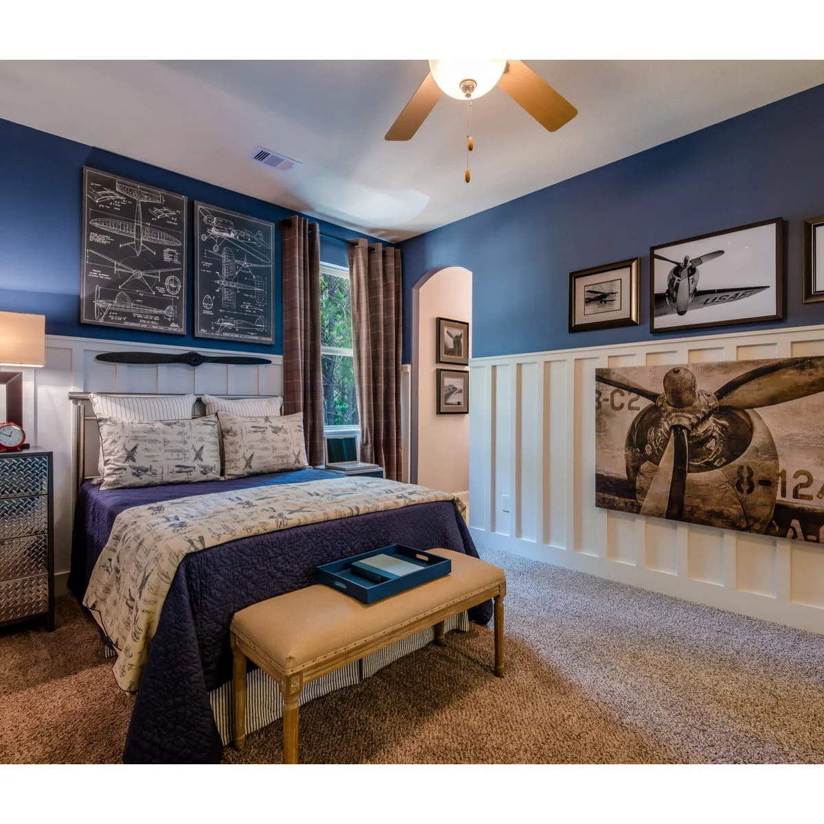 Blue boy’s bedroom with white lower wall panels, airplane artwork and a bench at the bed foot
