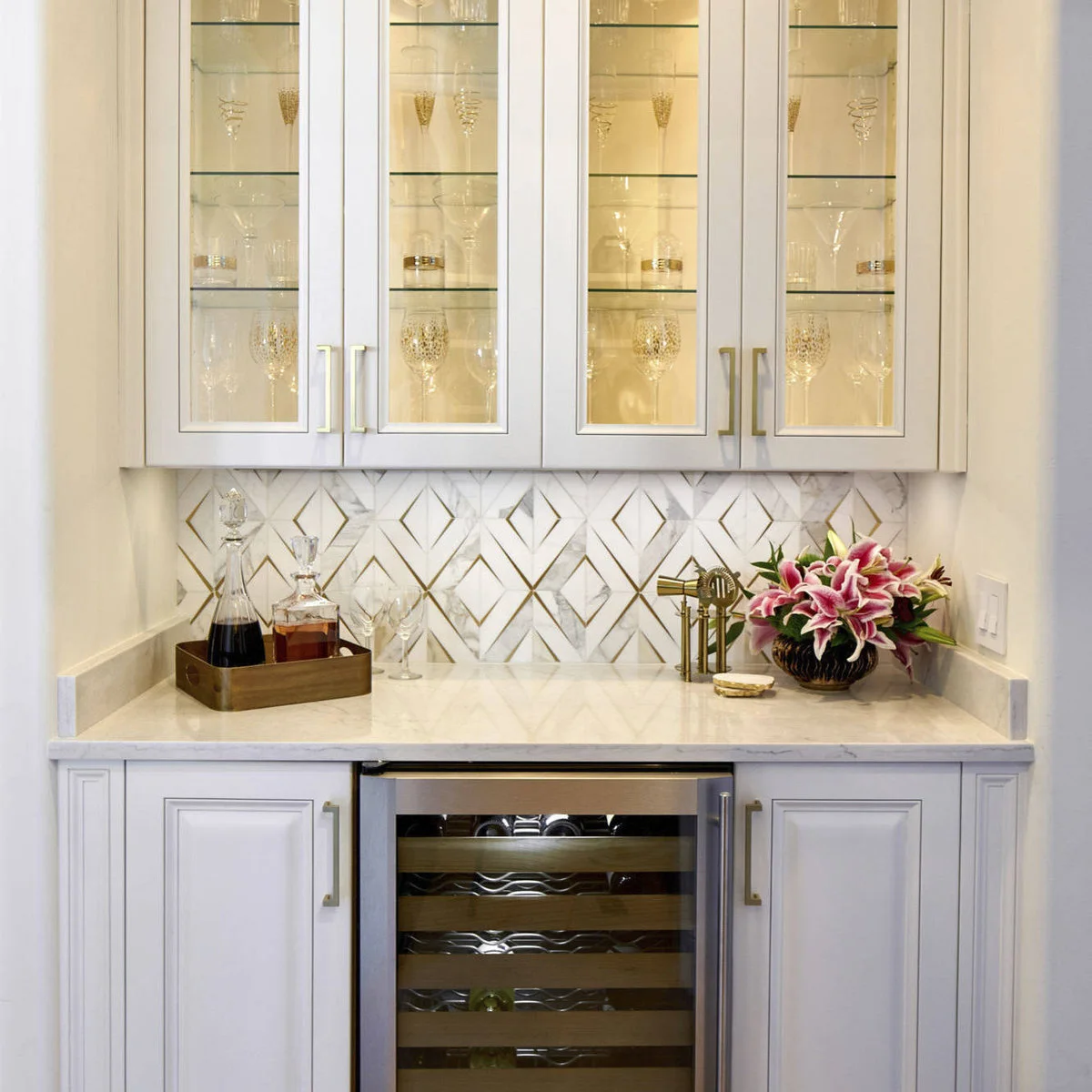 White mini bar with diamond-pattern backsplash, gold-toned details, lit glass cupboards and wine refrigerator