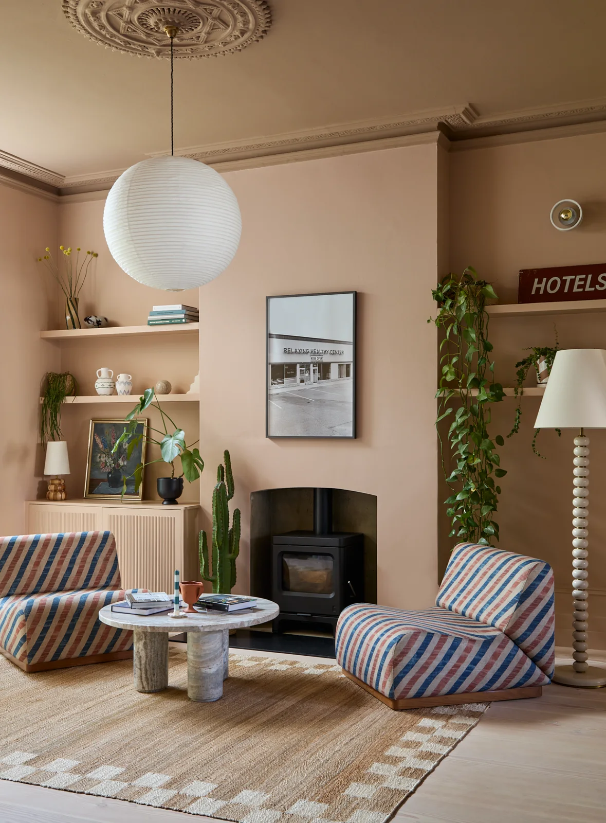 Peach-colored shelves and ridged cabinet fronts flank a fireplace, with trailing plants, lamps and framed art above the storage.