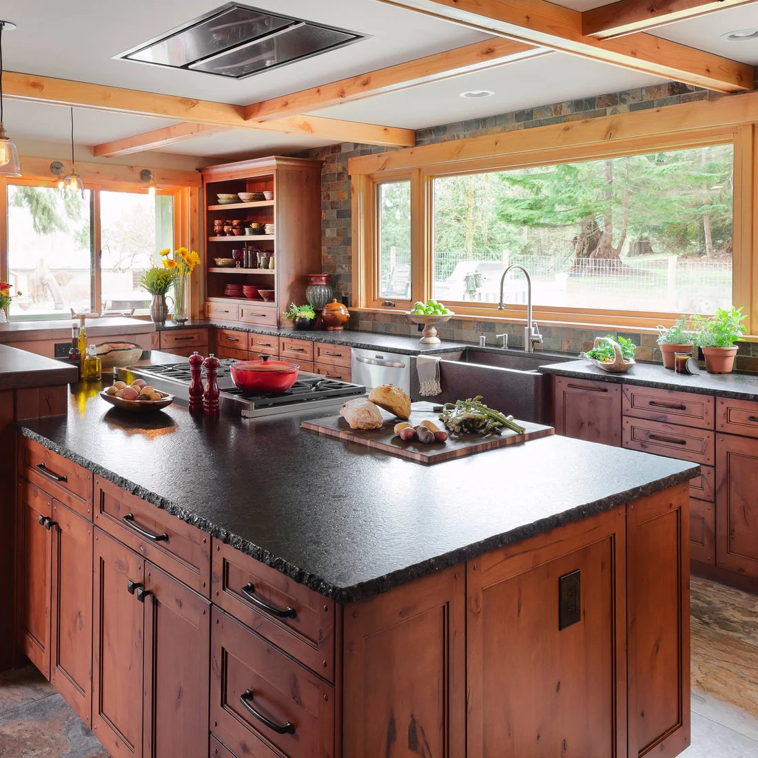 Timber cabinets and dark counters around a large sink window with an island cooktop