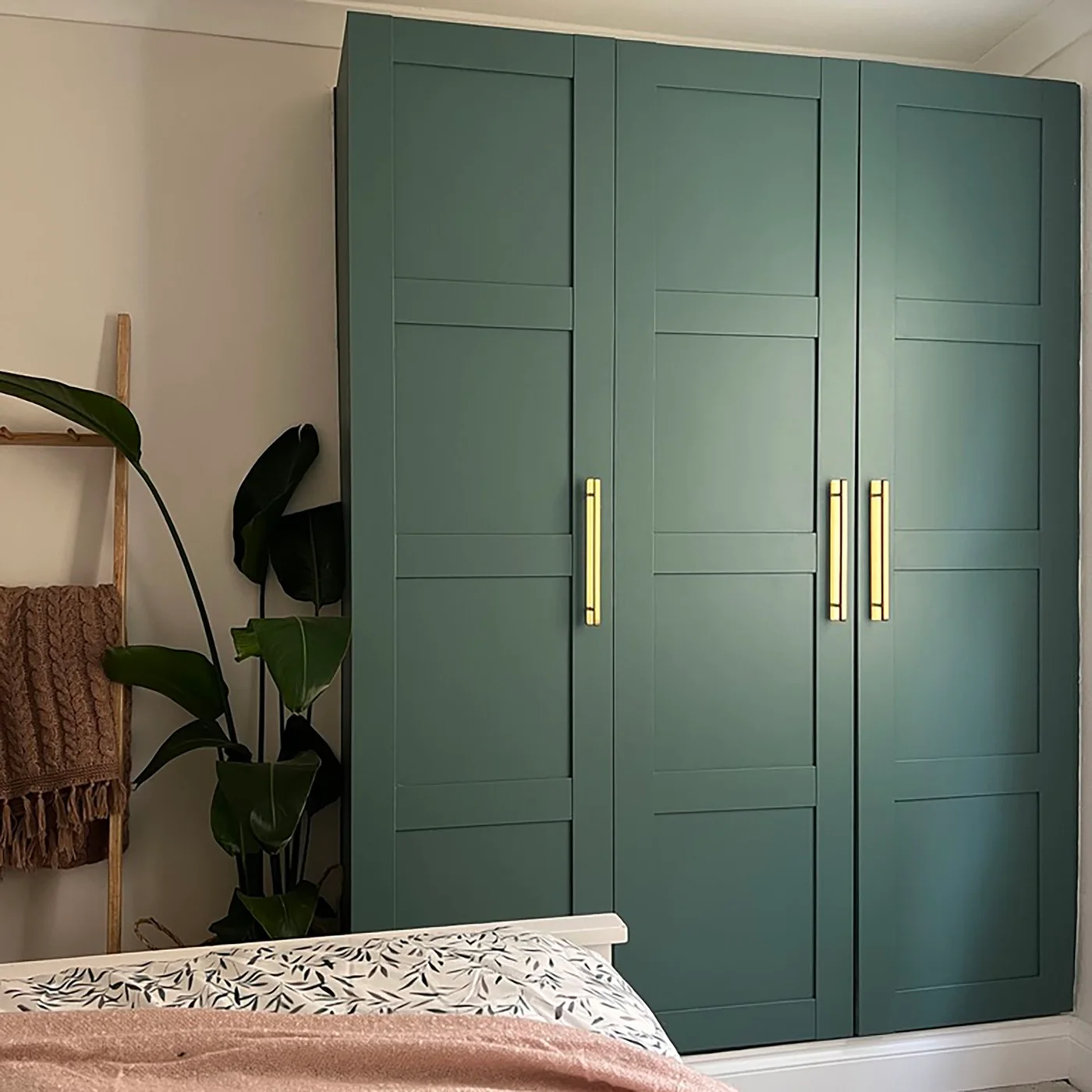 Blue-green PAX wardrobe with paneled doors and long gold-colored handles beside a bed