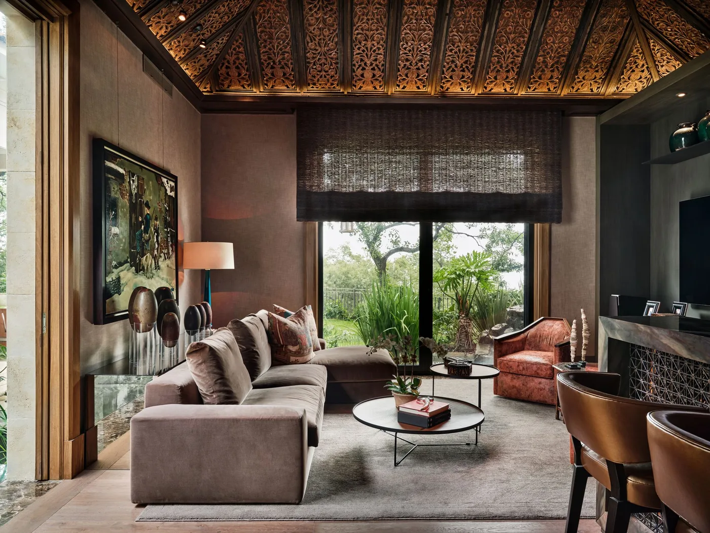 Warm brown living room beneath a patterned vaulted ceiling with pale sectional, rust armchair and dark round tables