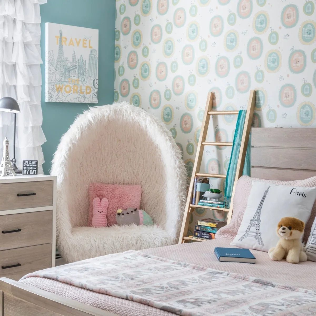 Bedroom with pale pink bedding, a light teal wall, white egg-shaped chair, patterned wall area and ladder storage