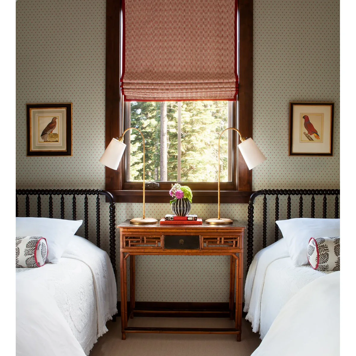 Two dark spindle beds with white covers, shared wood table, paired adjustable lamps and red window shade