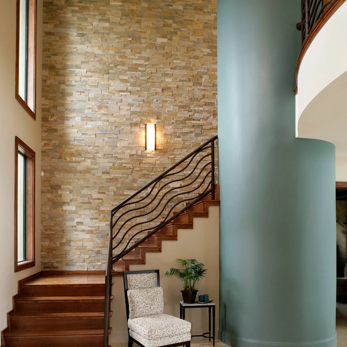 A warm stacked-stone wall rises behind wood stairs and a dark sculptural railing.