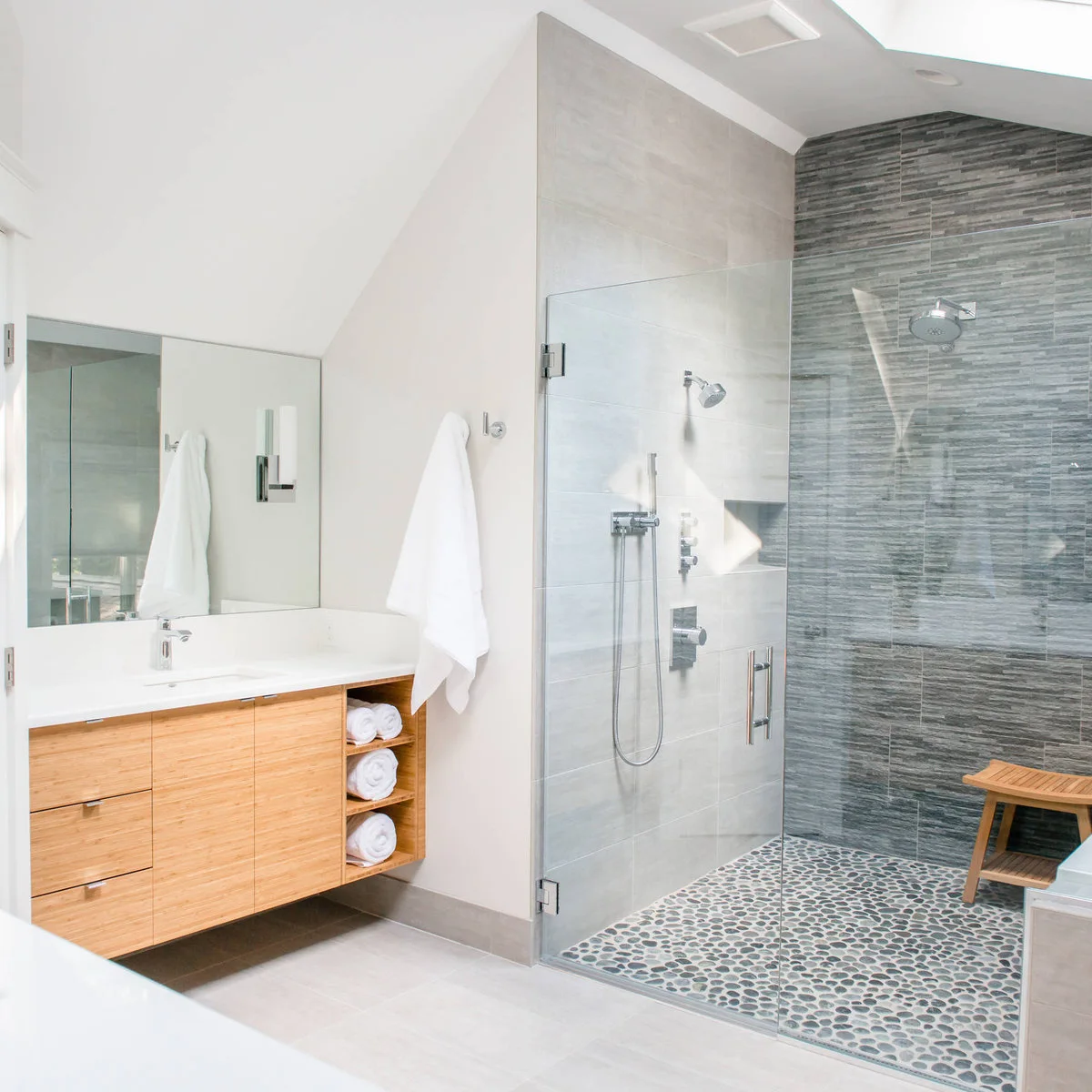 Tall glass shower with pebble-pattern floor and a small slatted wood stool