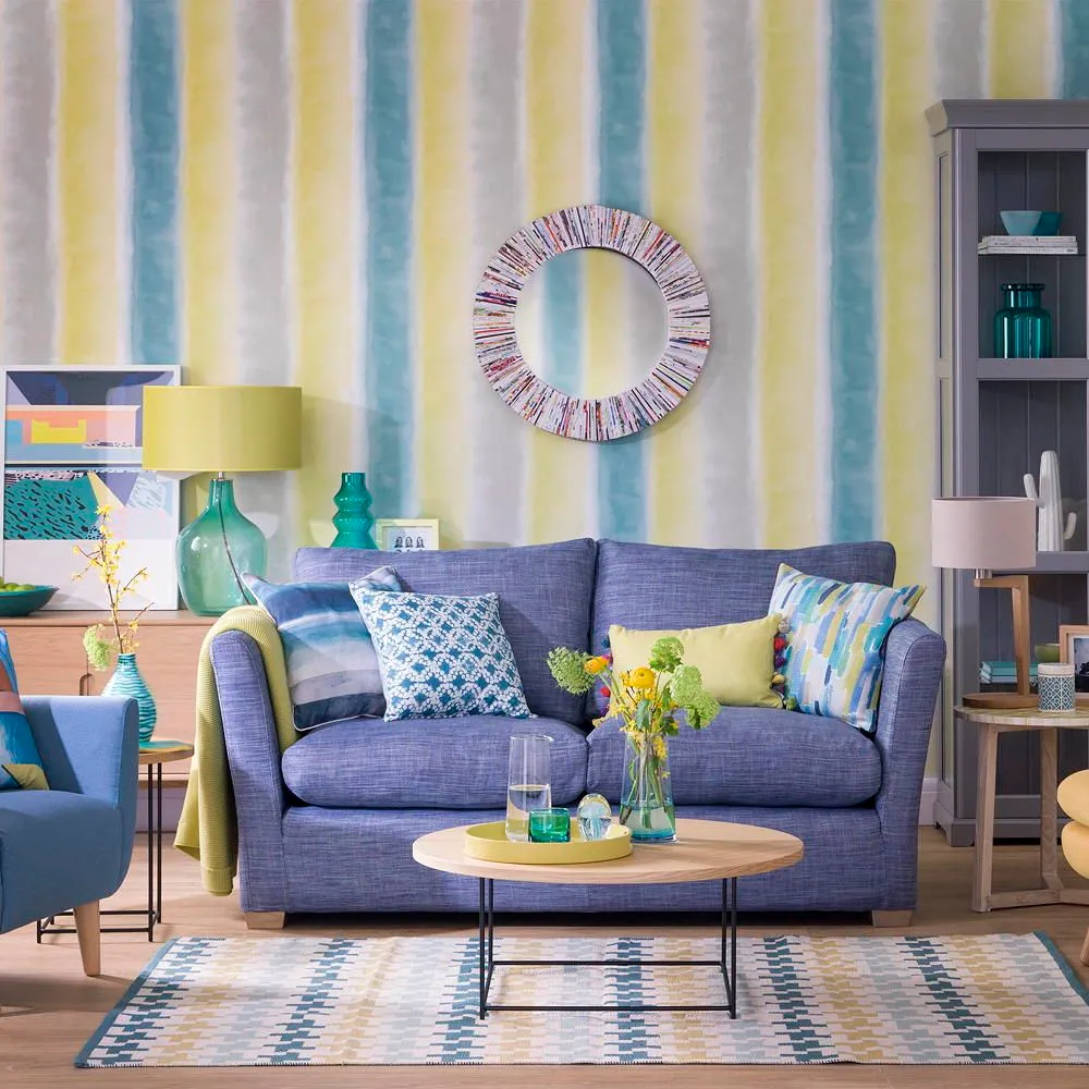 A blue sofa sits beneath pale multicolored stripes beside a round timber table.