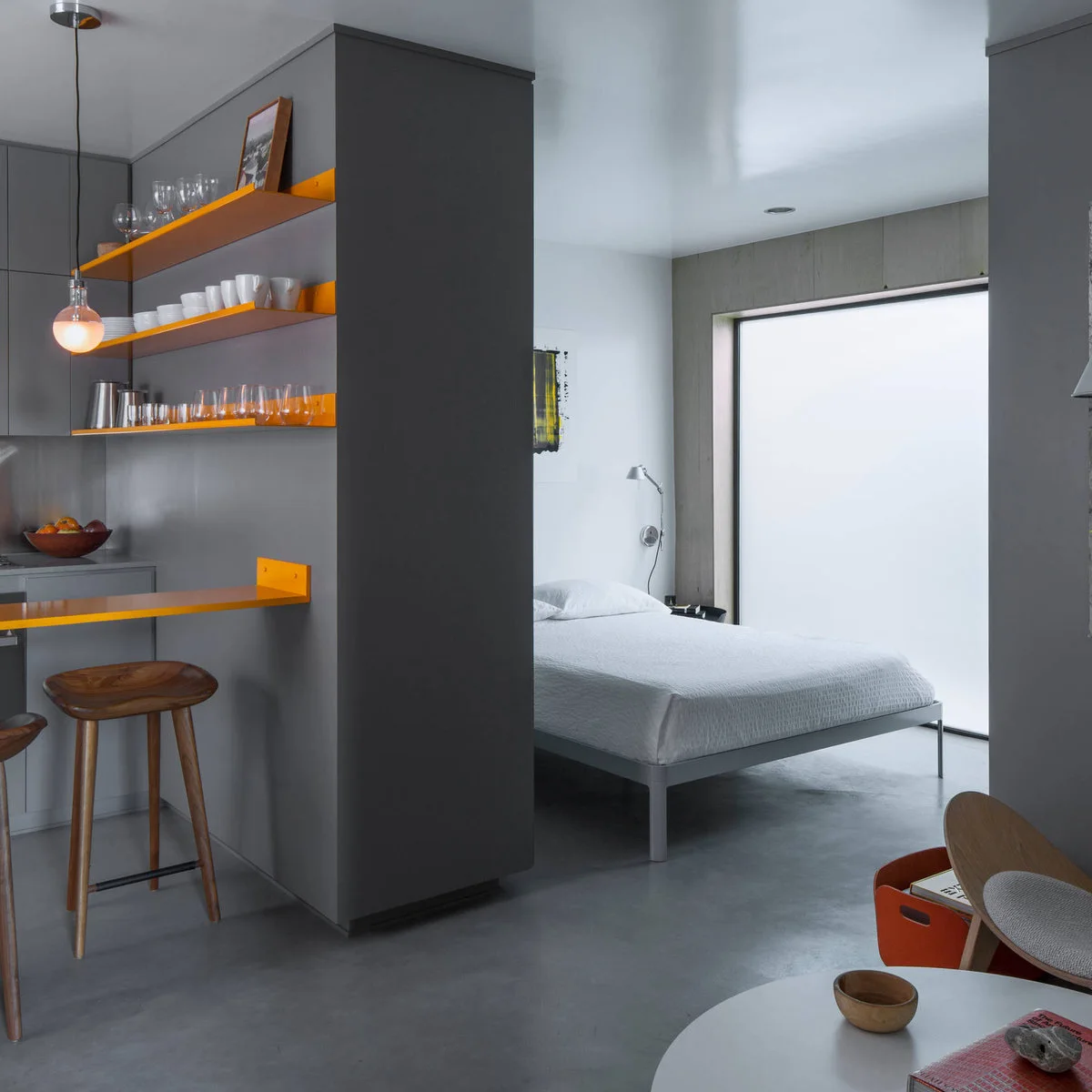 Micro-apartment with orange shelves of plates and glasses on the kitchen side of a dark partition