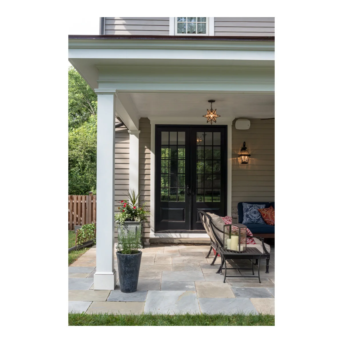 Covered stone front porch with black glazed doors, a white column and two tall planters