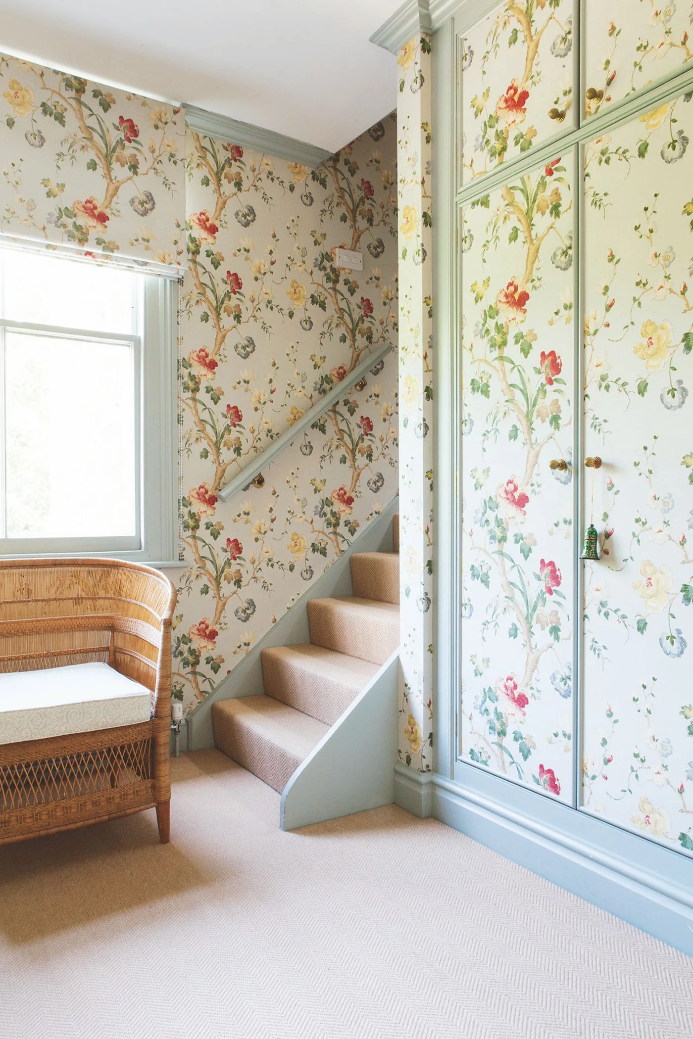 Country stair hall with pale floral wallpaper repeated inside painted cupboard door panels