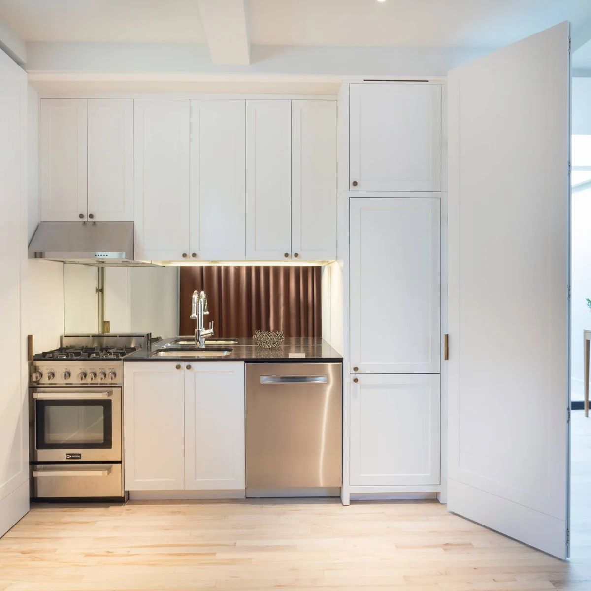 Compact white one-wall kitchen with tall pantry cabinet and metallic backsplash
