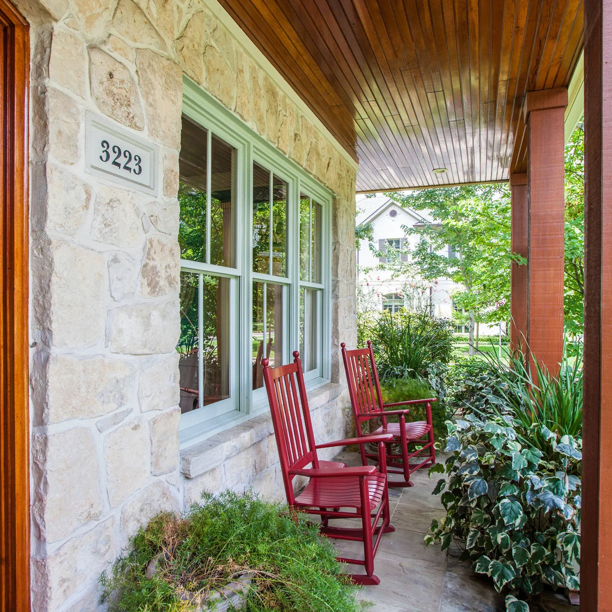 Two red rocking chairs against a stone front wall beneath a wood-colored porch ceiling
