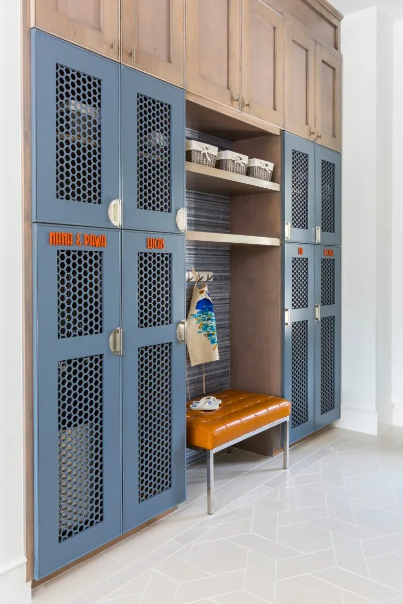 An orange tufted bench sits in a wood-lined recess between tall blue perforated locker doors and upper cupboards.