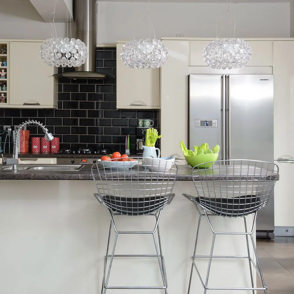 Warm off-white cabinets surround a black tiled backsplash beneath three glass pendants