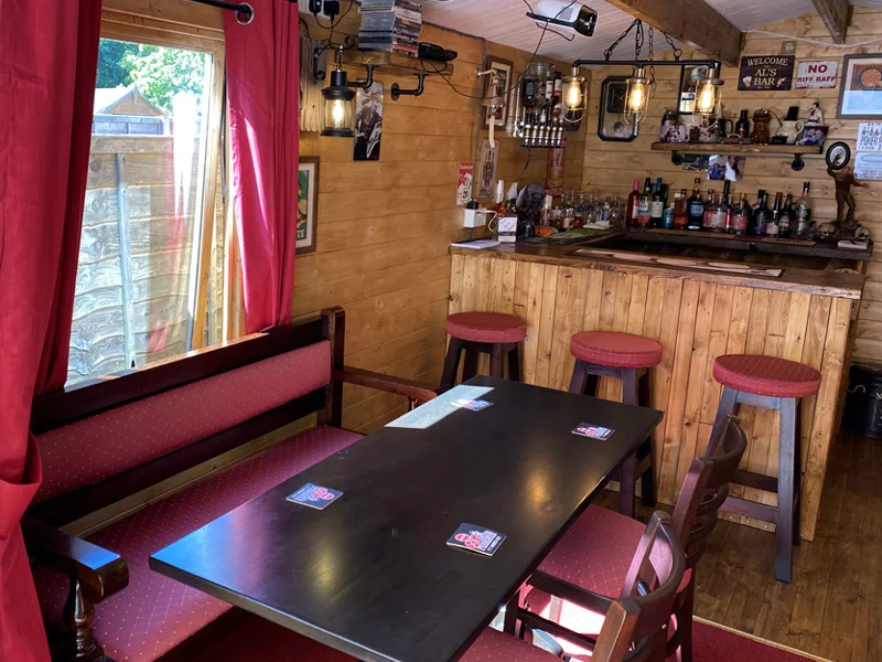 Wood shed pub with a dark rectangular table, red upholstered bench seating and bar stools