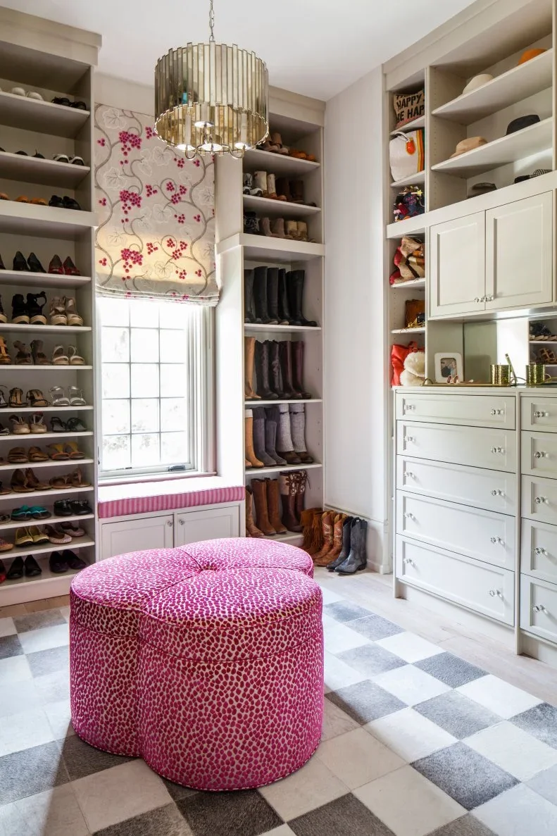 White closet shelving holds shoes and tall boots beside a window and a bright pink upholstered ottoman.