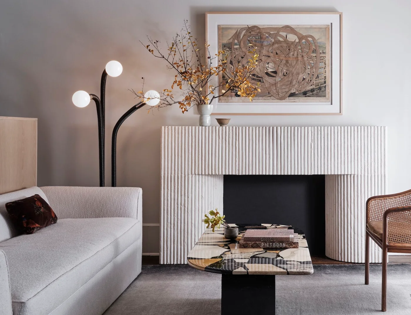 A pale vertically ridged fireplace surround stands below framed artwork beside a white sofa, black globe lamp and patterned coffee table