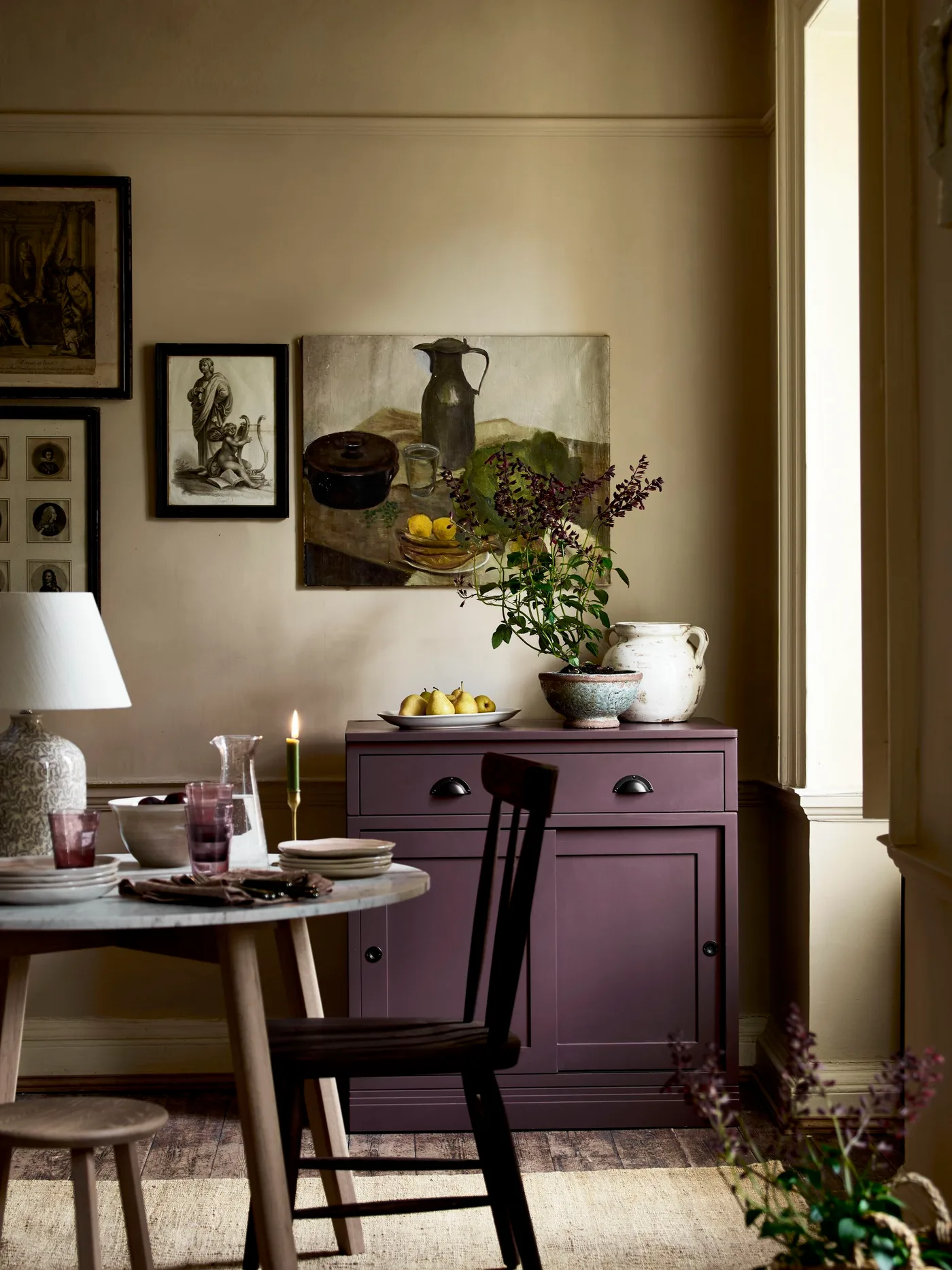 Small purple dining sideboard with a drawer and cupboard beneath grouped pictures beside a pale round table