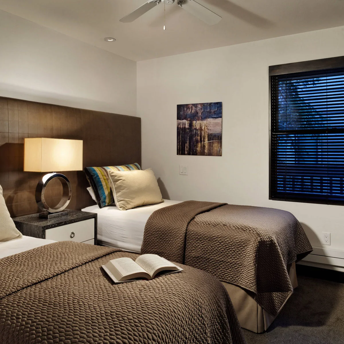 Twin sleeping arrangement with brown textured covers, compact bases, shared drawer table and broad brown headboard