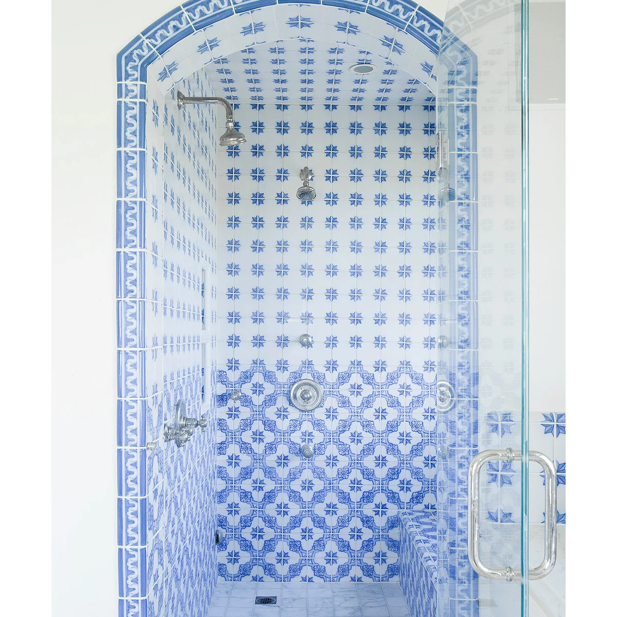 Arched shower covered in blue-and-white star and floral tiles with blue border trim