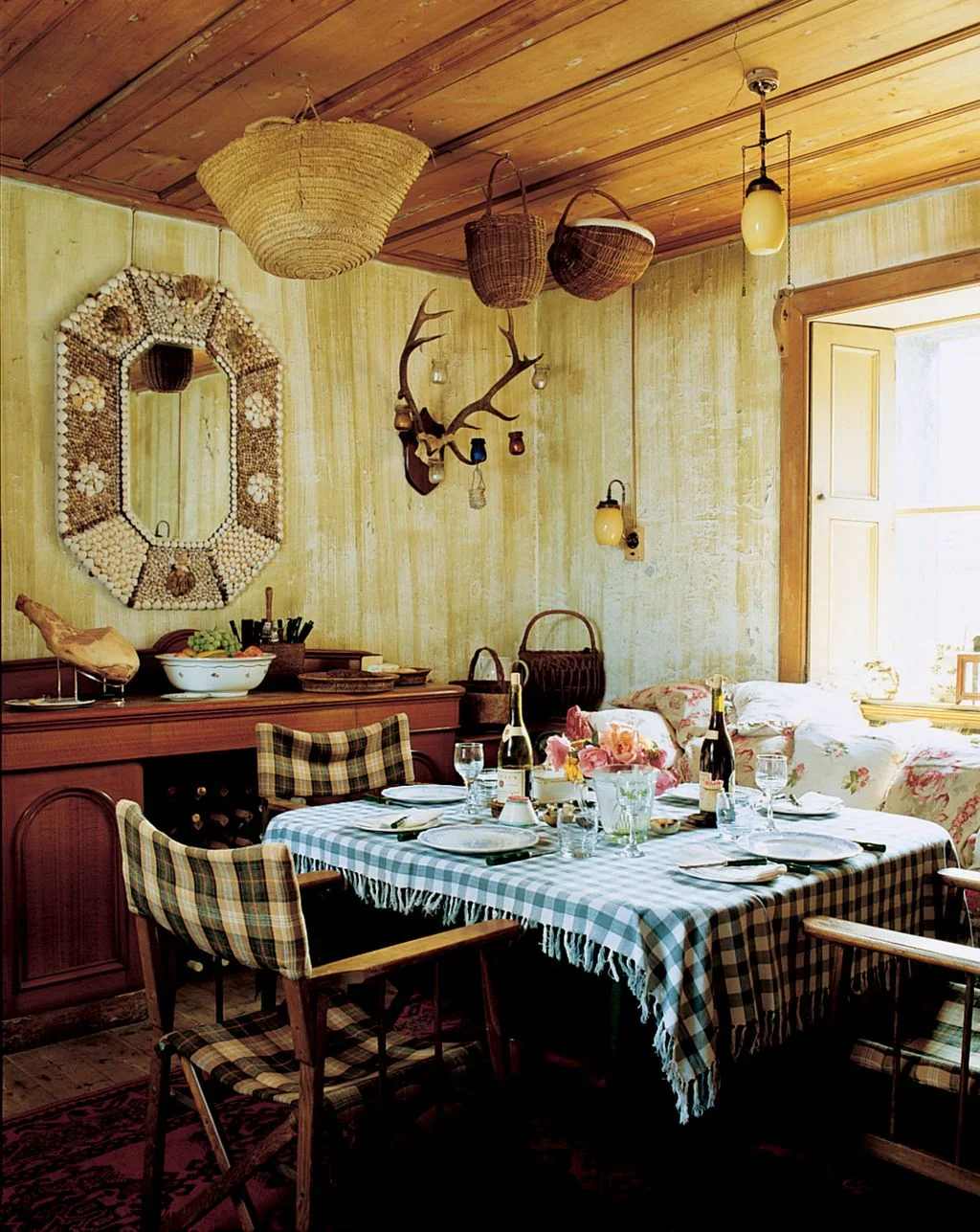 Country dining room with checked upholstered chairs, a blue checked tablecloth and woven baskets overhead