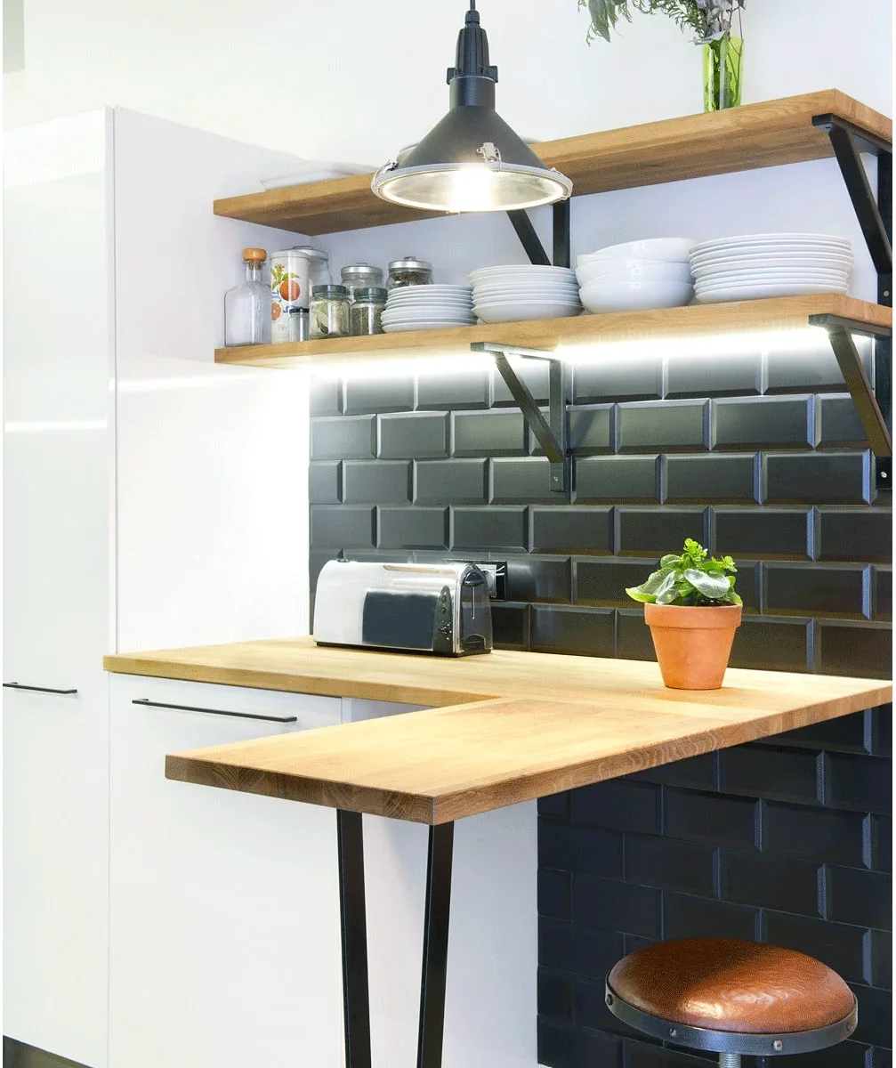 A bright strip beneath a wood shelf lights a compact wood counter with black beveled tiles and a dark pendant above.
