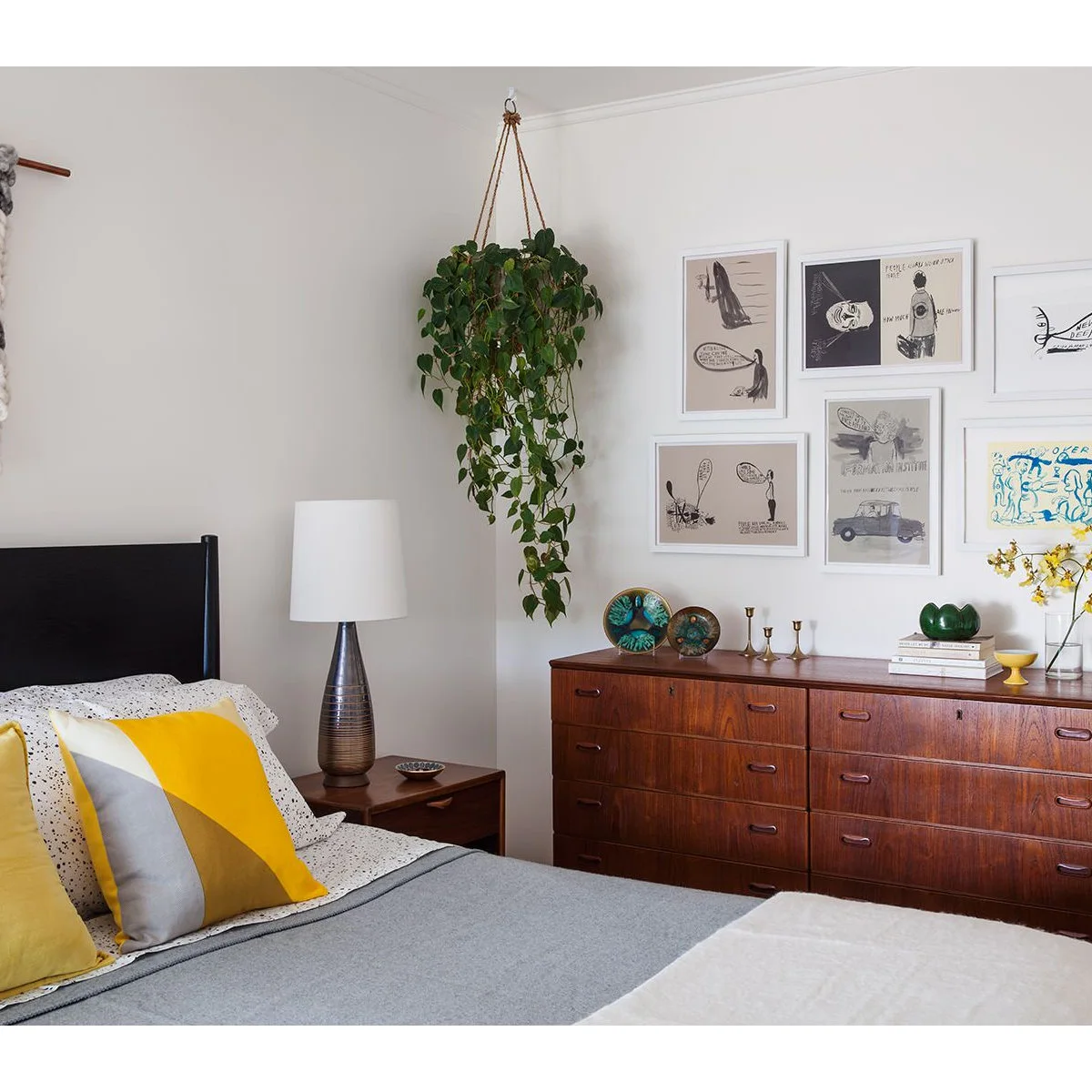 Bedroom with a long wood-colored dresser, framed illustrations and a yellow accent pillow