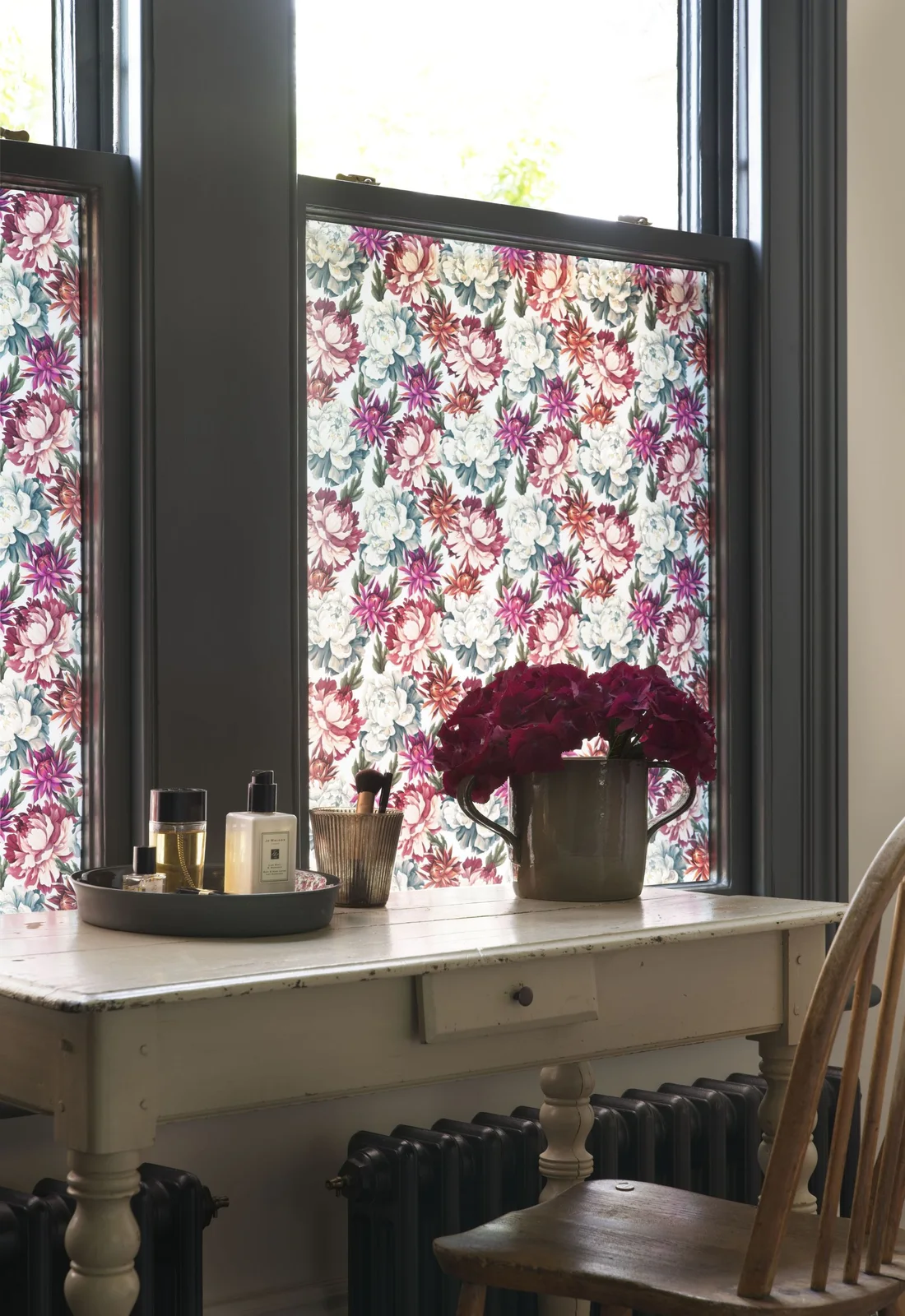 A small tray of toiletries and a brush holder sit on a pale table beside floral window panels