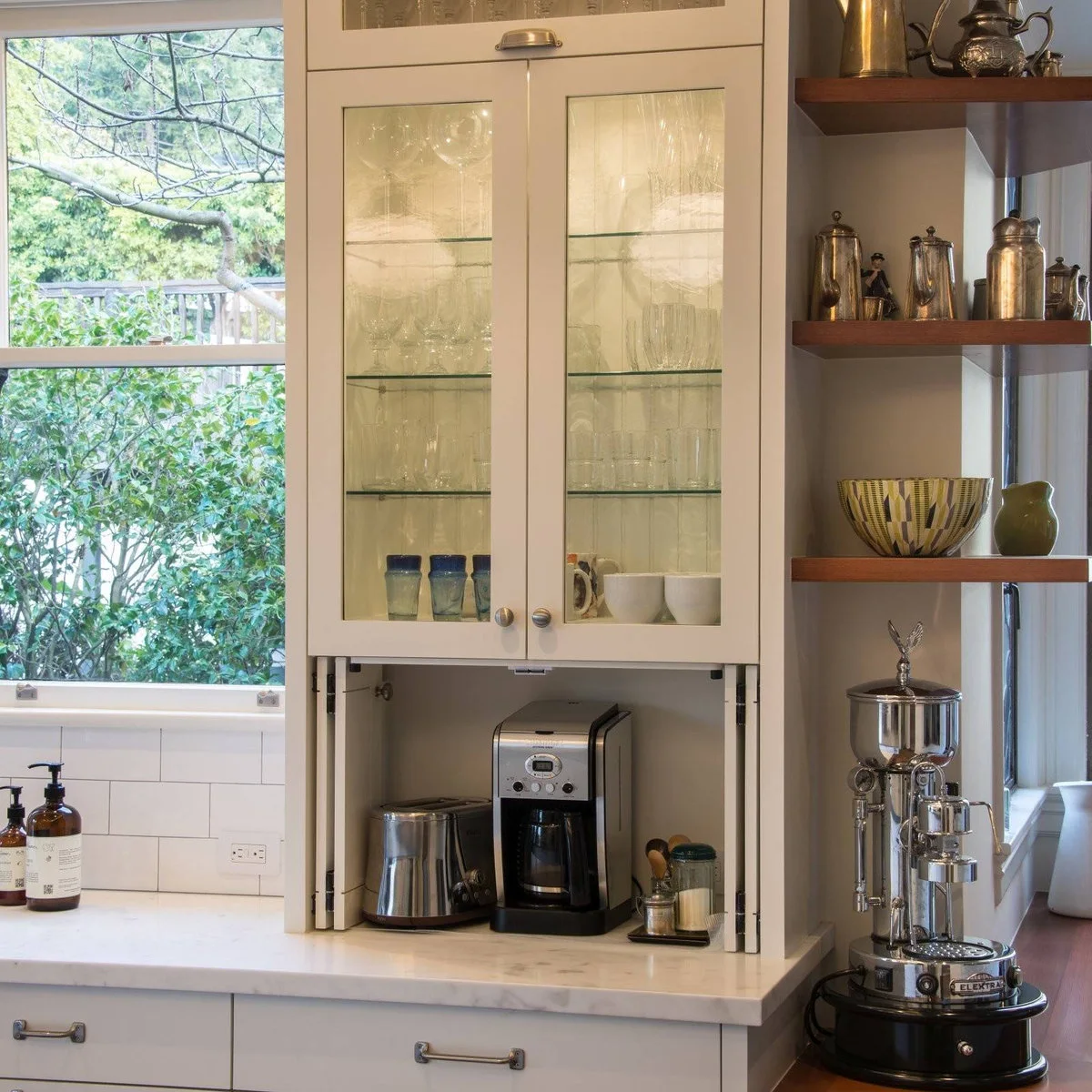 White coffee cabinet beneath glazed glassware storage with coffee machine, toaster and small supply tray