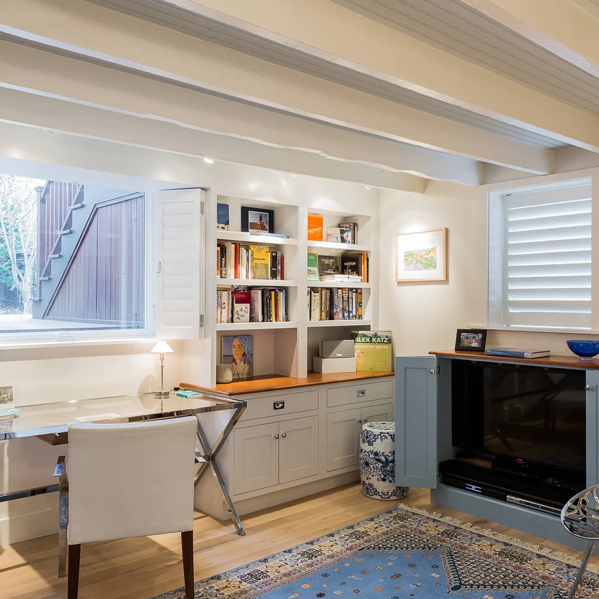 A reflective desk beside built-in shelves and a blue cabinet with open doors revealing a television.
