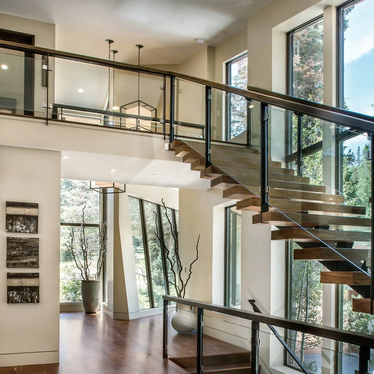 Open staircase with wood treads, dark-framed glass guards and tall windows beside the flight