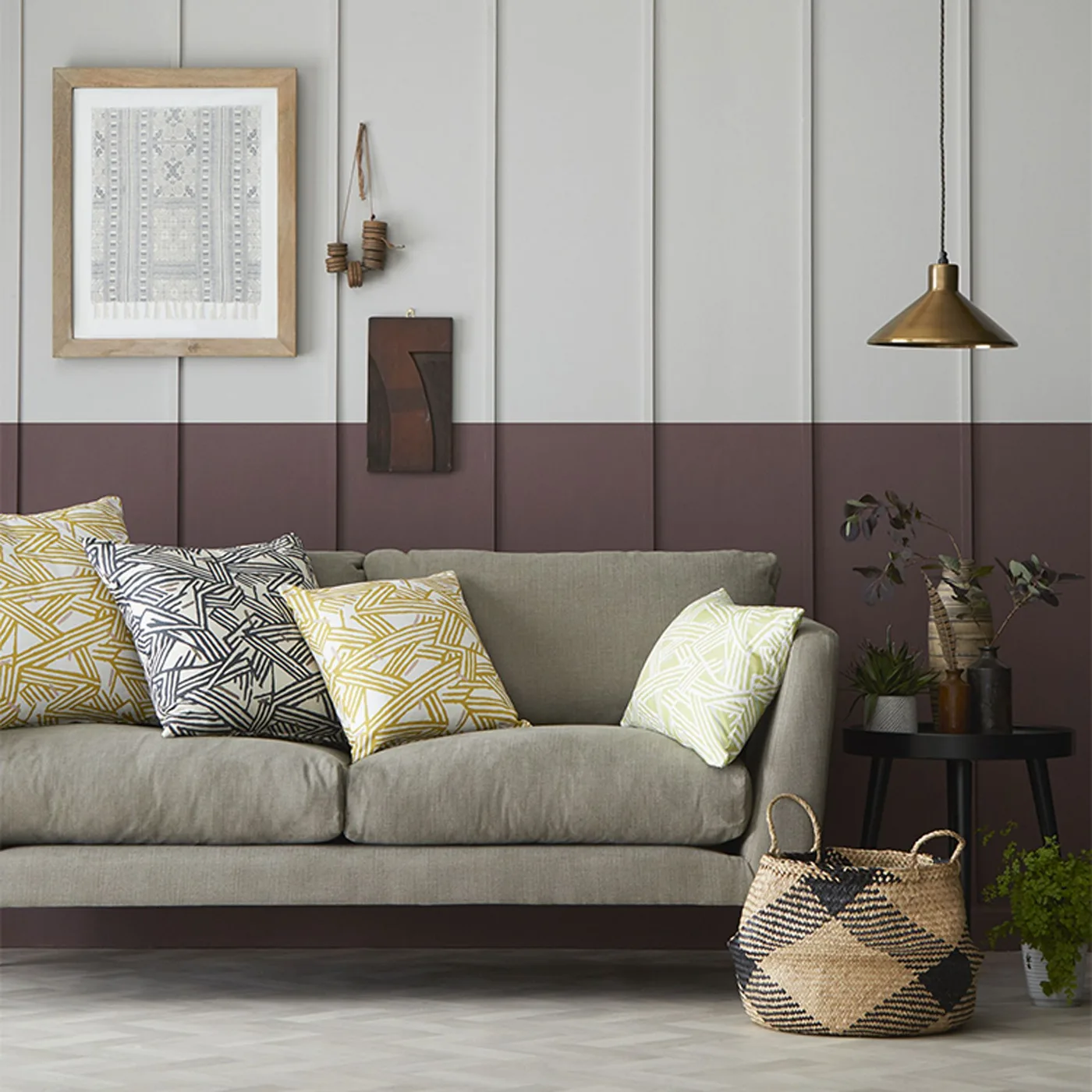 Pale gray couch with yellow and dark geometric pillows beneath two-tone paneled walls.