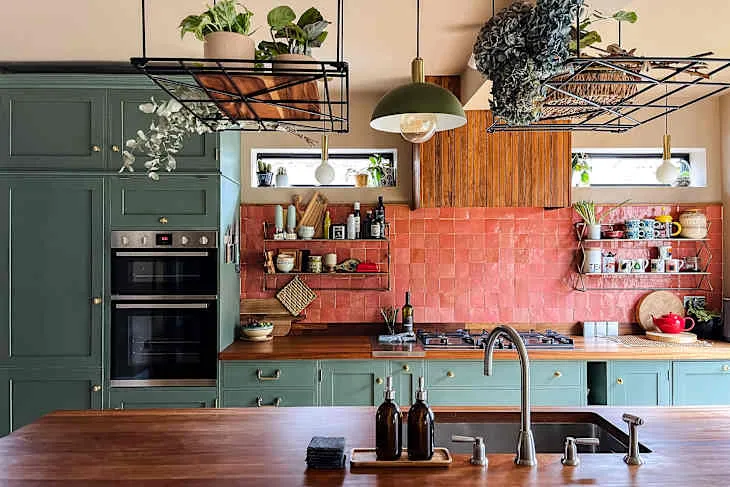 Deep green shaker cabinets, salmon-pink zellige-style backsplash, wooden counter and hanging plants