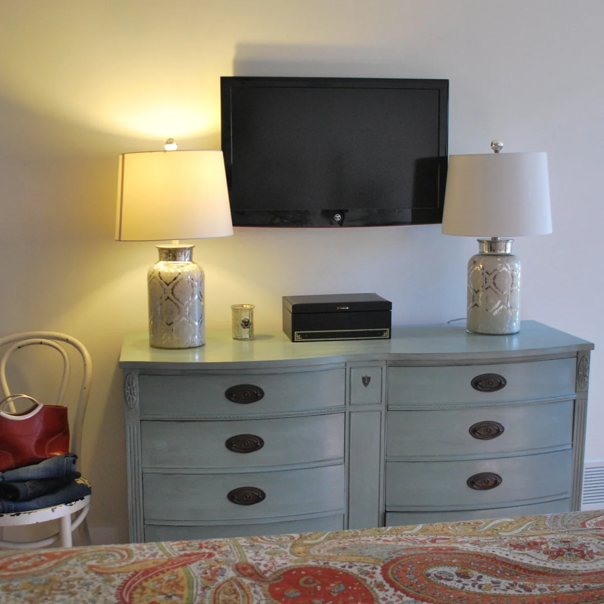 Pale blue curved-front dresser beneath a television with two matching lamps