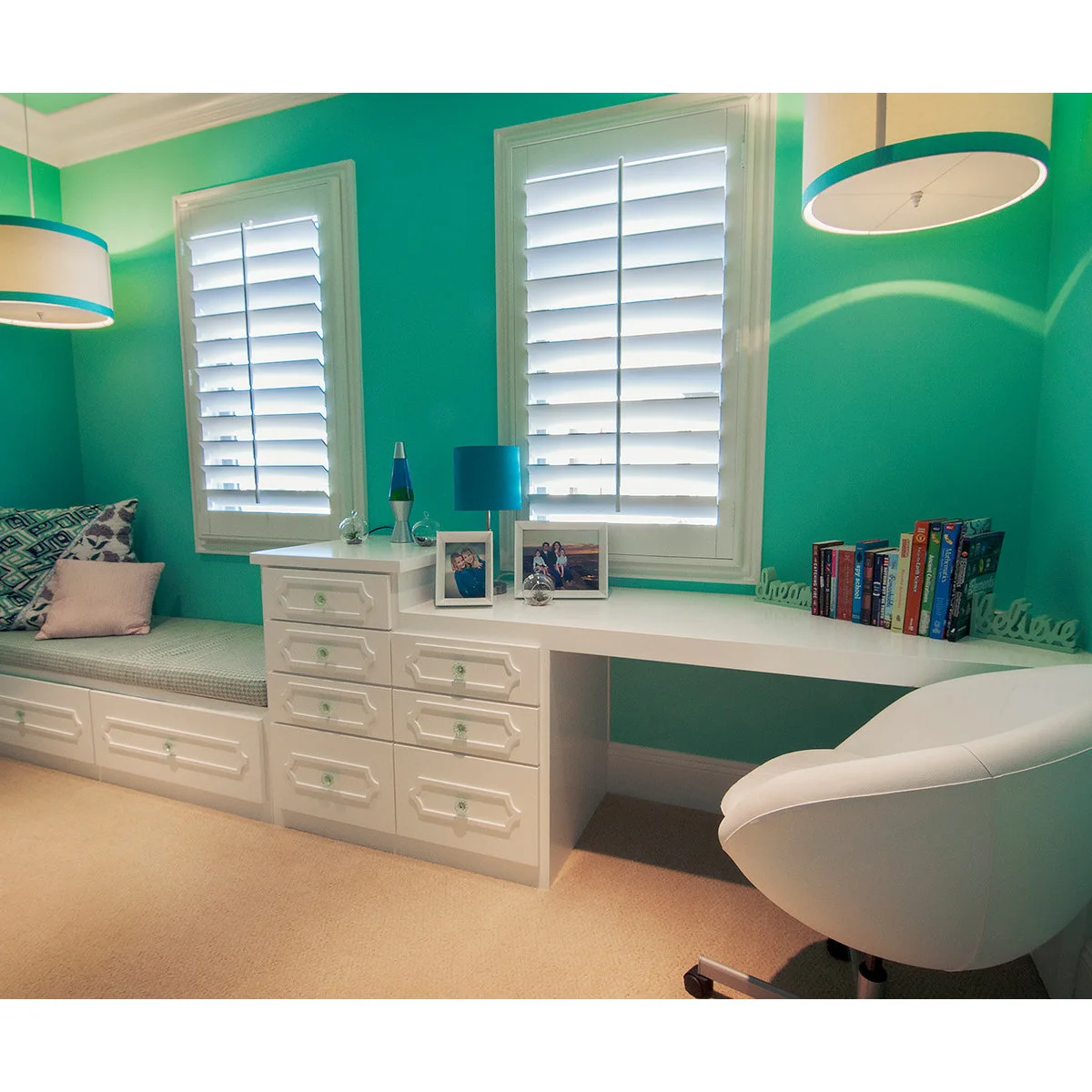 Turquoise bedroom with a white built-in desk, drawer chest and cushioned window seat