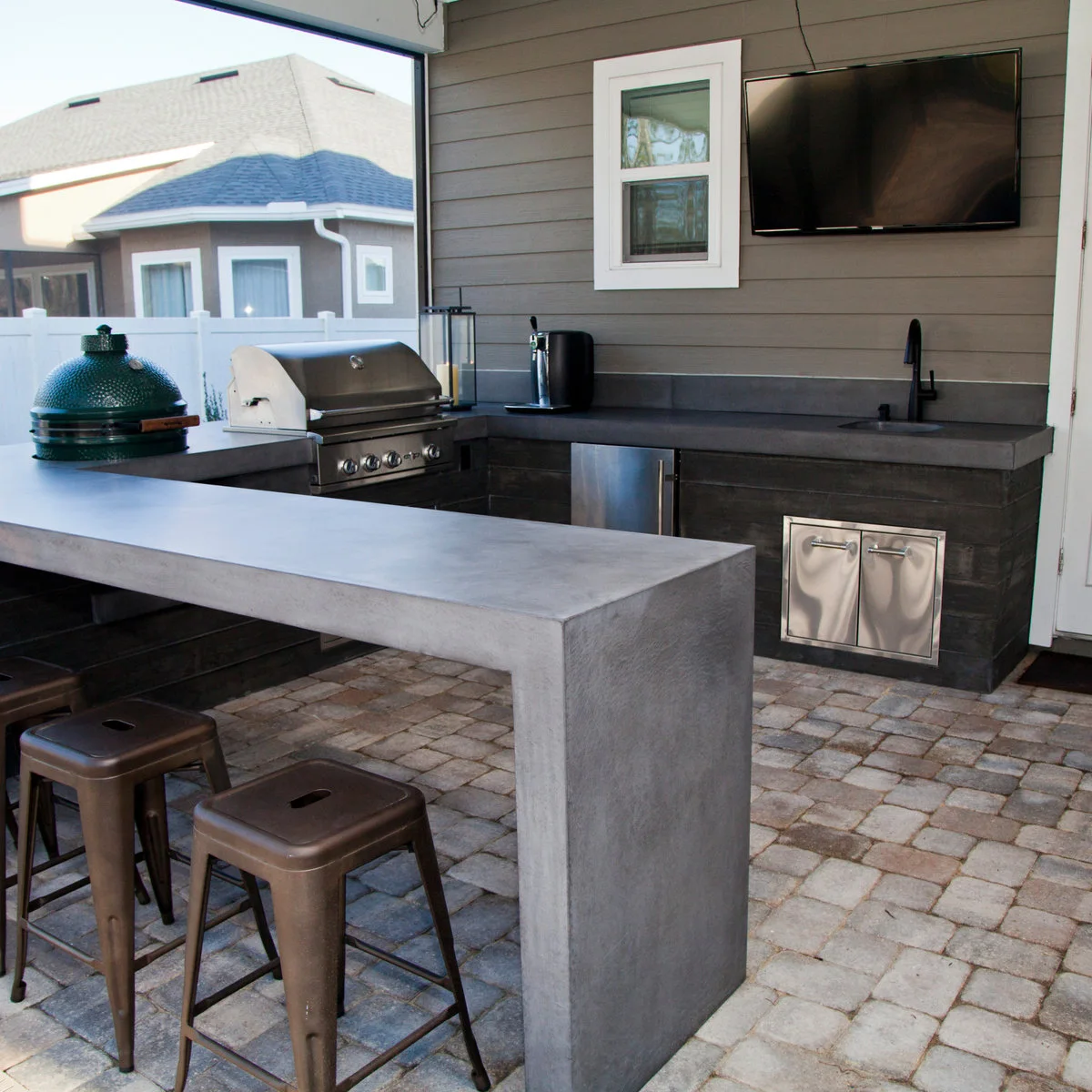 Gray outdoor kitchen with a sink along the back counter, corner grill and separate counter-height seating ledge