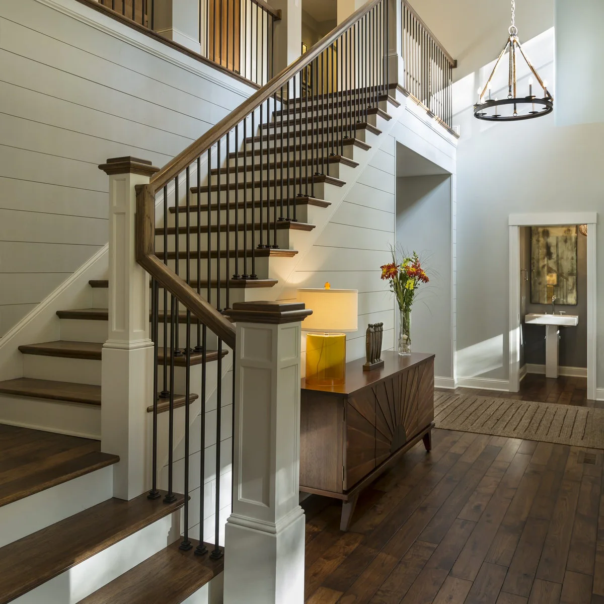 White staircase with dark vertical balusters beside horizontally boarded walls and a wood entry cabinet
