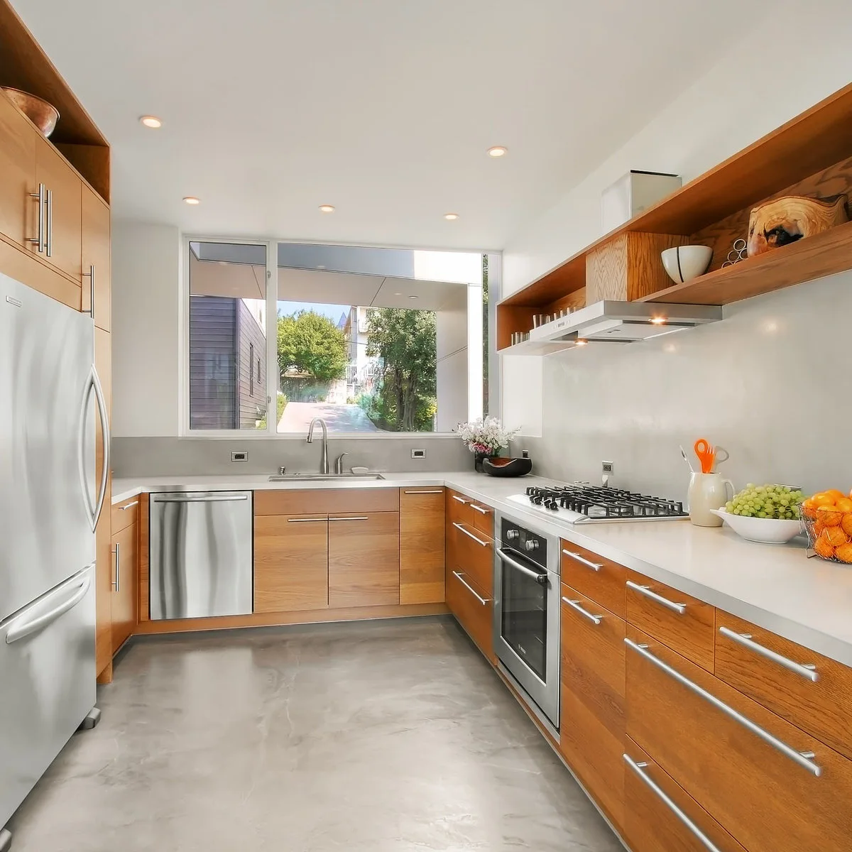 A broad picture window above a sink in a wood-and-white kitchen with simple counters and open side shelves.
