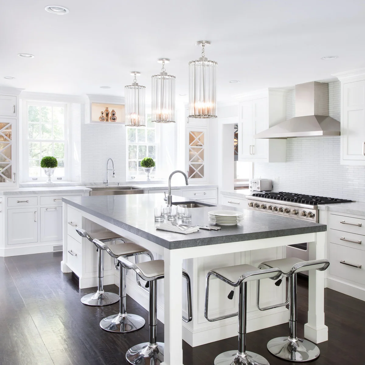 Pale low-backed pedestal stools with shiny metal bases and rectangular footrests around a white island
