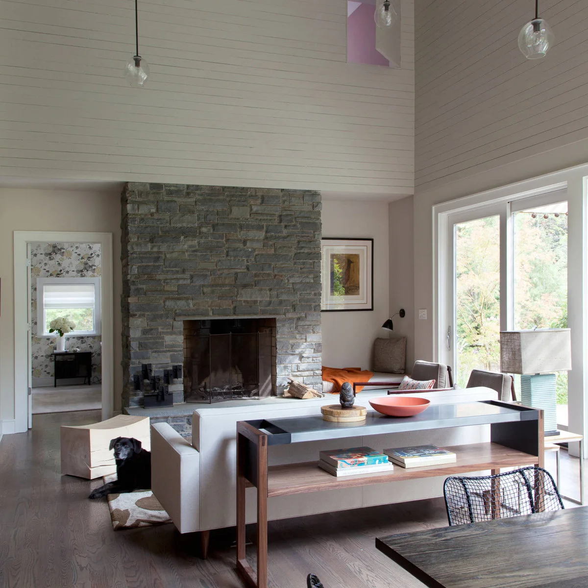 White sofa facing a stone fireplace with a narrow open console behind it and a table beyond