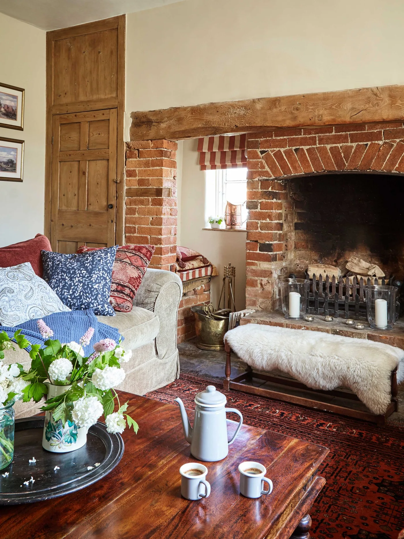 Brick fireplace with unlit candles, low fluffy-covered bench, patterned cushions and wood coffee table
