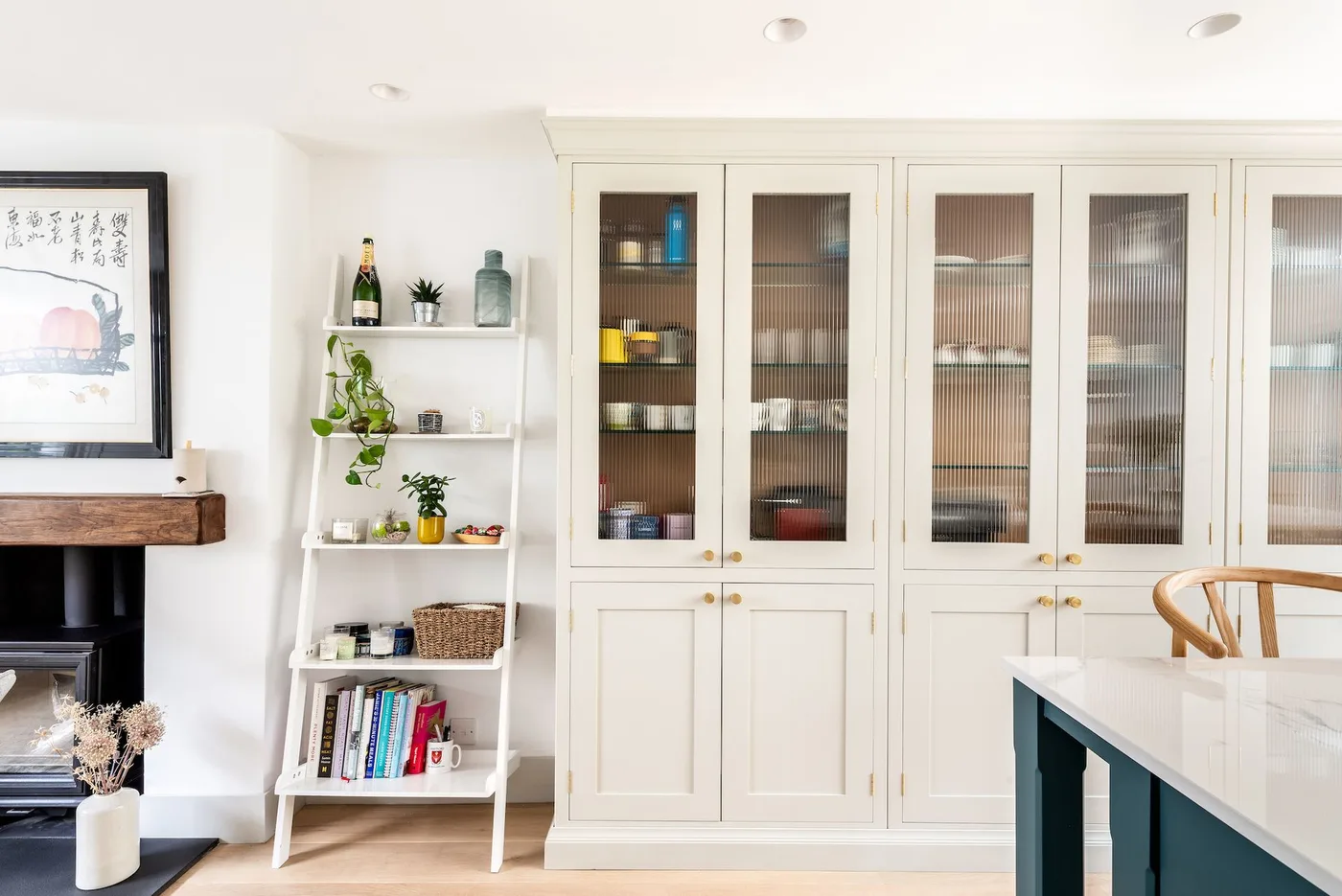 Tall pale kitchen cabinets with textured glazed upper doors, visible dishes, narrow open shelves and dark island edge.