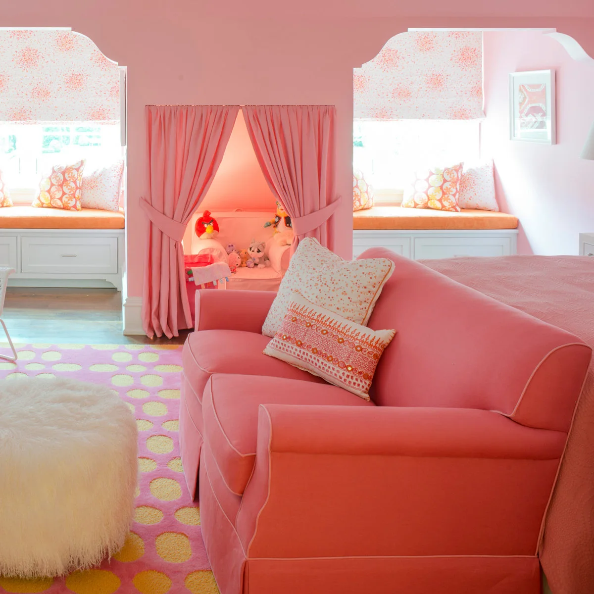 Pink upholstered chair with white piping near window seats and a curtained play nook
