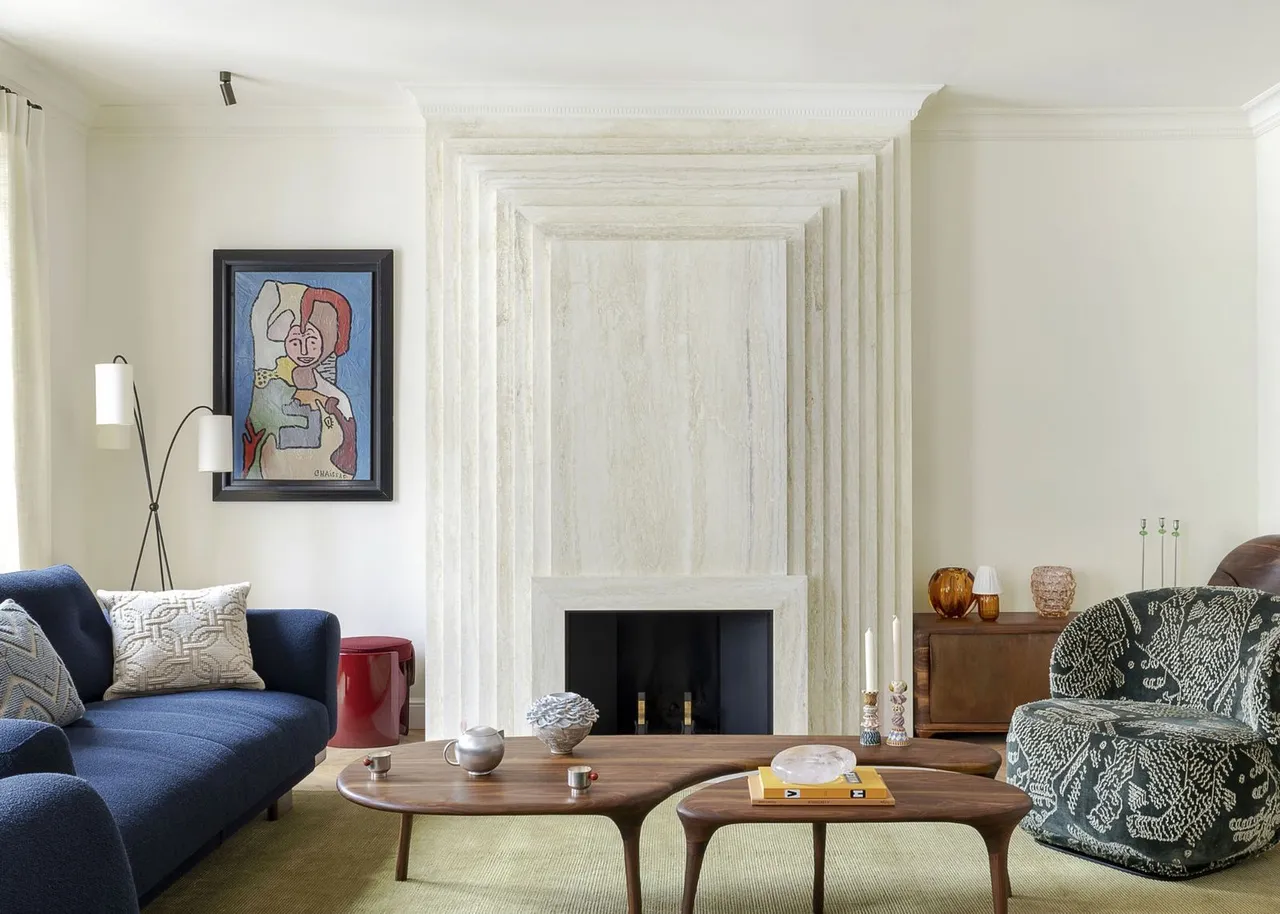 A navy sofa sits beside a green patterned armchair and pale fireplace.
